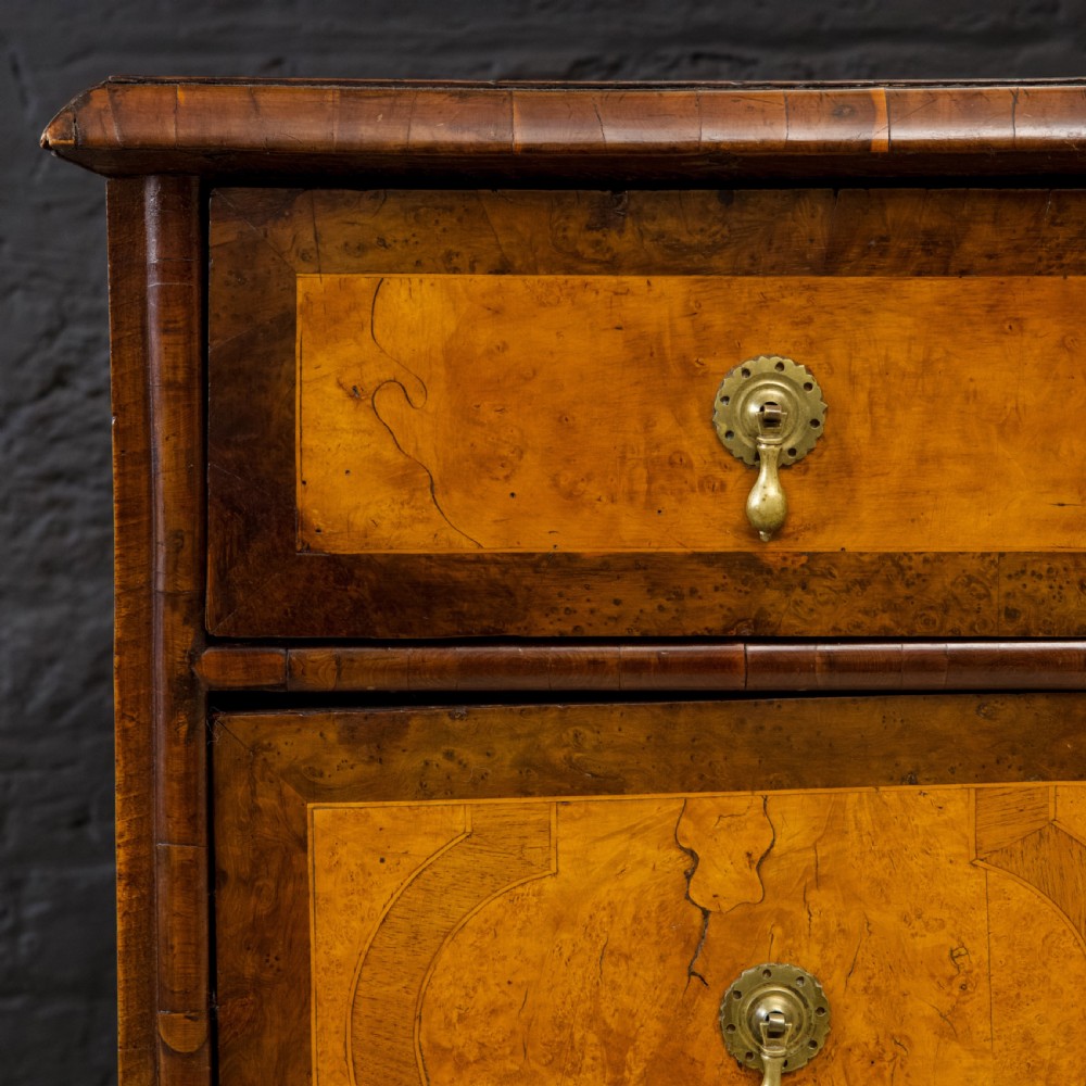 A late 17th-century William and Mary chest of drawers crafted from yew and maple featuring geometric inlaid panels, teardrop brass handles, and turned bun feet. View VI