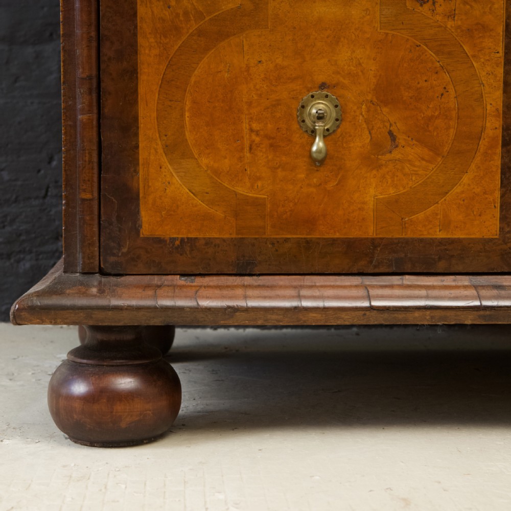 A late 17th-century William and Mary chest of drawers crafted from yew and maple featuring geometric inlaid panels, teardrop brass handles, and turned bun feet. View VII