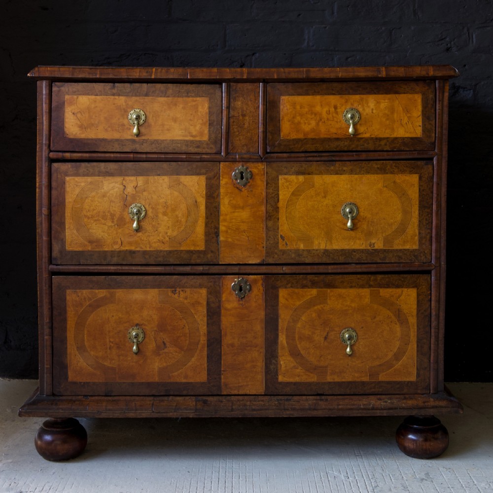 A late 17th-century William and Mary chest of drawers crafted from yew and maple featuring geometric inlaid panels, teardrop brass handles, and turned bun feet. View XVII