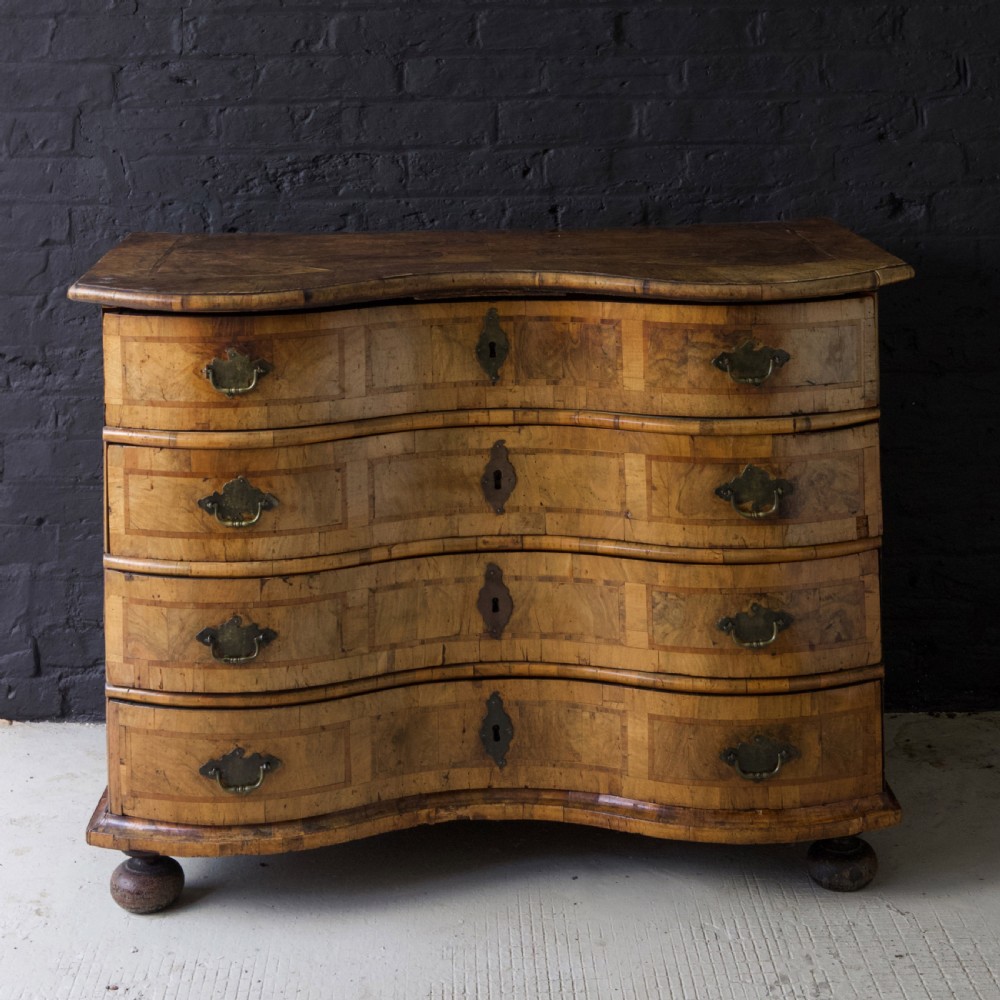 An 18th-century South German walnut chest of drawers featuring a serpentine front, four crossbanded drawers, brass drop handles, and turned bun feet. View V