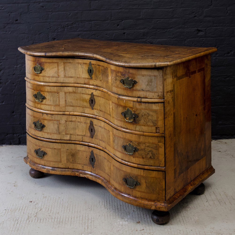 An 18th-century South German walnut chest of drawers featuring a serpentine front, four crossbanded drawers, brass drop handles, and turned bun feet. View VII