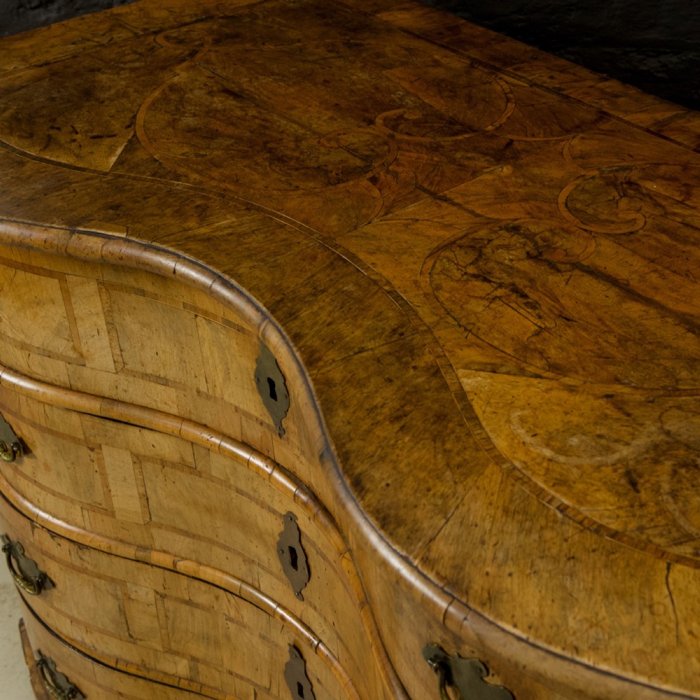 An 18th-century South German walnut chest of drawers featuring a serpentine front, four crossbanded drawers, brass drop handles, and turned bun feet. View IX