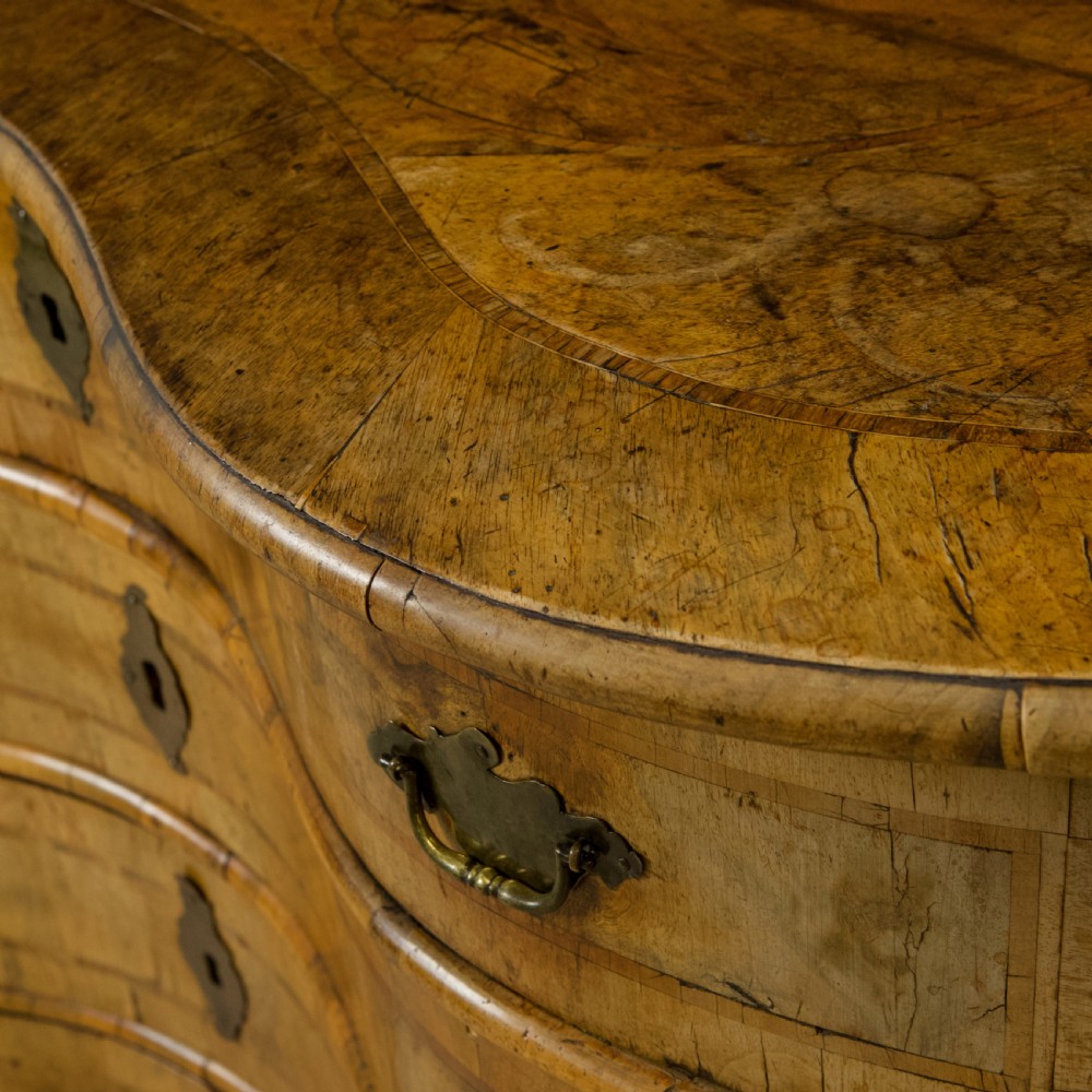 An 18th-century South German walnut chest of drawers featuring a serpentine front, four crossbanded drawers, brass drop handles, and turned bun feet. View X
