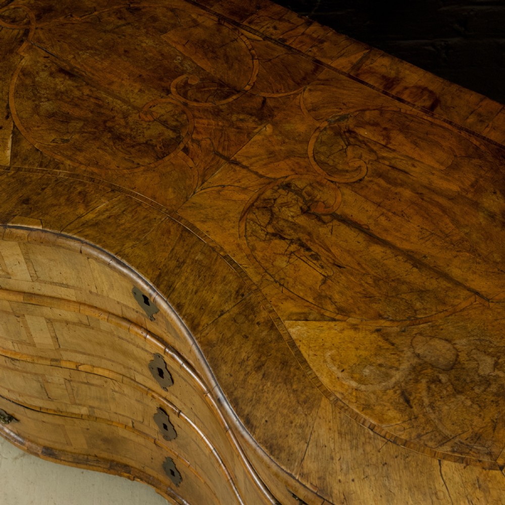 An 18th-century South German walnut chest of drawers featuring a serpentine front, four crossbanded drawers, brass drop handles, and turned bun feet. View XIV