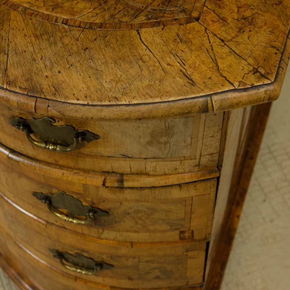 An 18th-century South German walnut chest of drawers featuring a serpentine front, four crossbanded drawers, brass drop handles, and turned bun feet. View XV