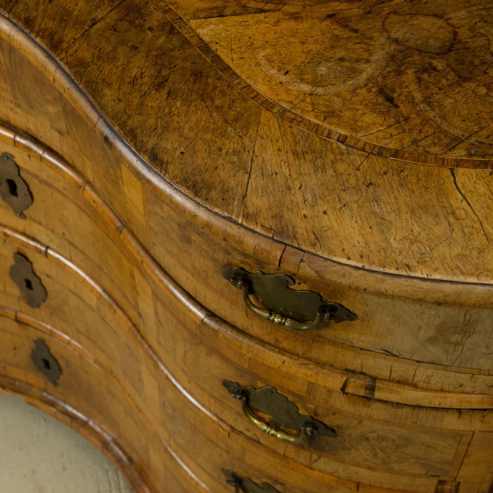 An 18th-century South German walnut chest of drawers featuring a serpentine front, four crossbanded drawers, brass drop handles, and turned bun feet. View XVI