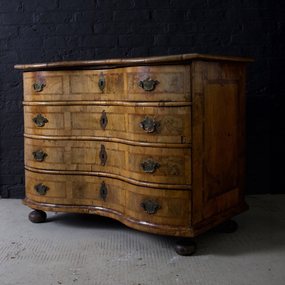 An 18th-century South German walnut chest of drawers featuring a serpentine front, four crossbanded drawers, brass drop handles, and turned bun feet. View XVII