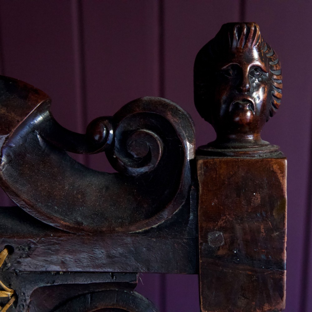 A 17th-century Carolean dark walnut armchair featuring a tall scroll-carved back with a central cane panel, scrolled armrests, and a grey upholstered seat. View VIII