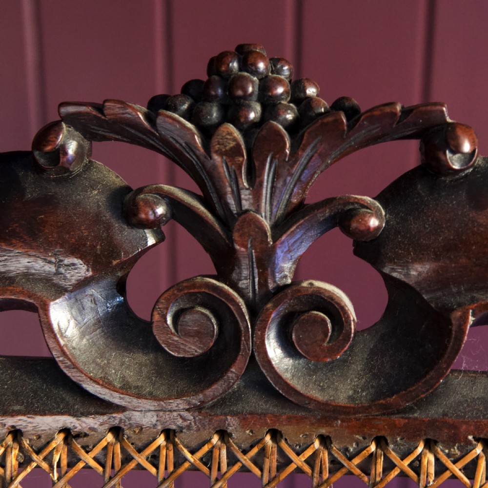 A 17th-century Carolean dark walnut armchair featuring a tall scroll-carved back with a central cane panel, scrolled armrests, and a grey upholstered seat. View IX