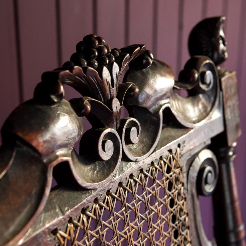 A 17th-century Carolean dark walnut armchair featuring a tall scroll-carved back with a central cane panel, scrolled armrests, and a grey upholstered seat. View X
