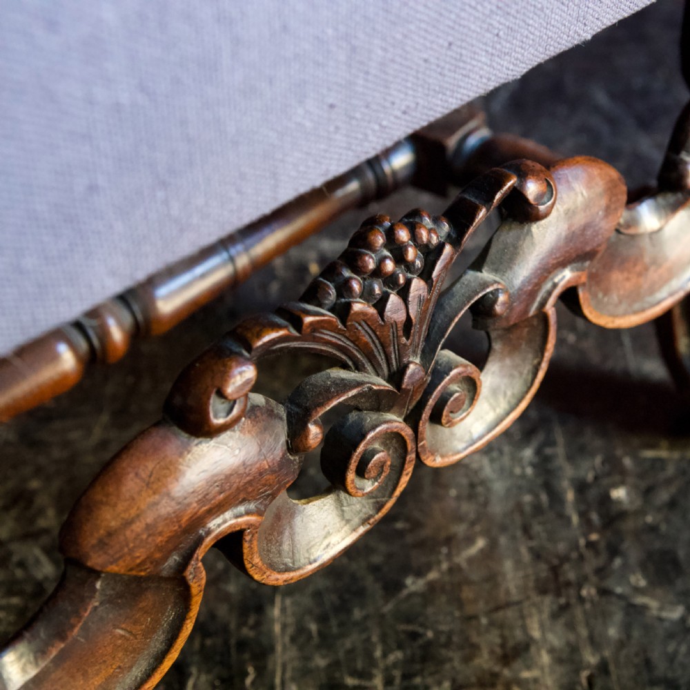 A 17th-century Carolean dark walnut armchair featuring a tall scroll-carved back with a central cane panel, scrolled armrests, and a grey upholstered seat. View XII