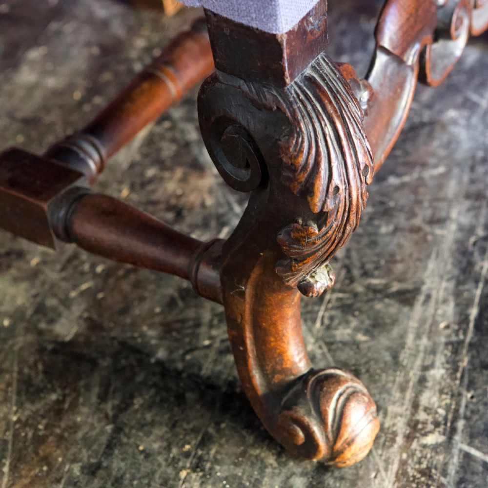 A 17th-century Carolean dark walnut armchair featuring a tall scroll-carved back with a central cane panel, scrolled armrests, and a grey upholstered seat. View XVIII