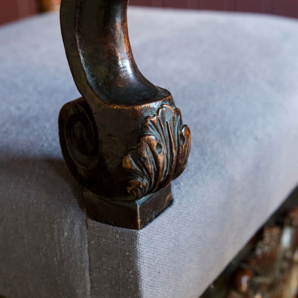 A 17th-century Carolean dark walnut armchair featuring a tall scroll-carved back with a central cane panel, scrolled armrests, and a grey upholstered seat. View XIX