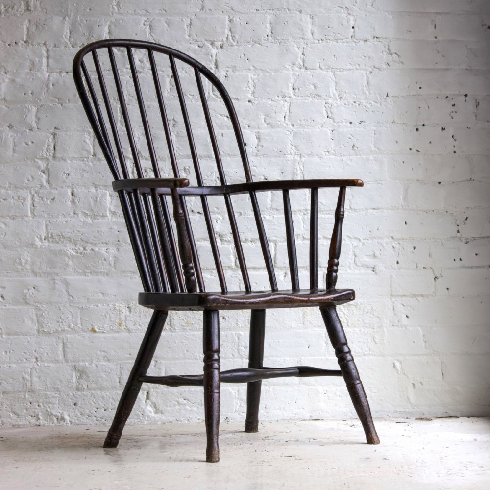 An 18th-century dark brown wooden stickback Windsor armchair featuring a tall curved hoop back, turned legs, and an H-stretcher. View II