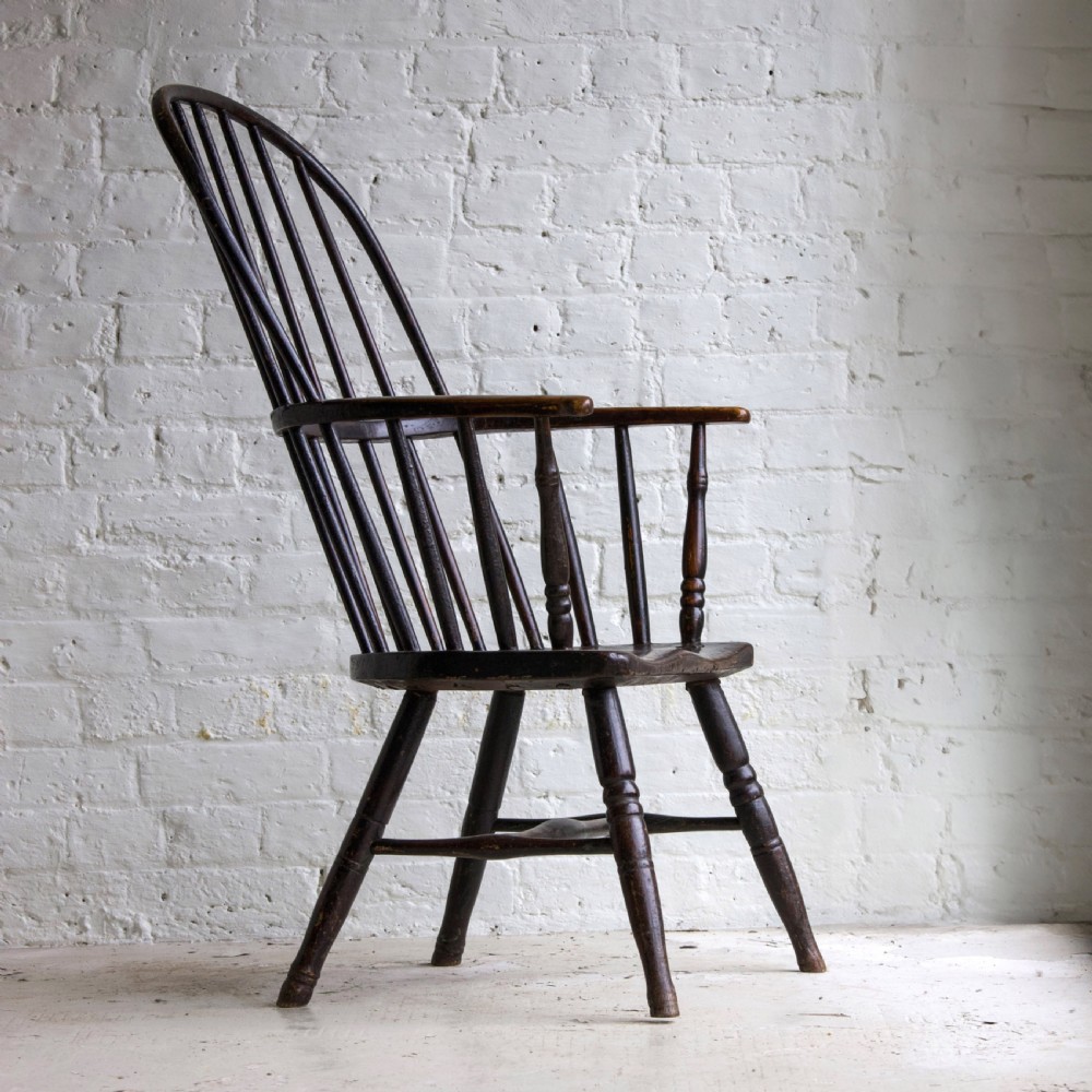 An 18th-century dark brown wooden stickback Windsor armchair featuring a tall curved hoop back, turned legs, and an H-stretcher. View VI