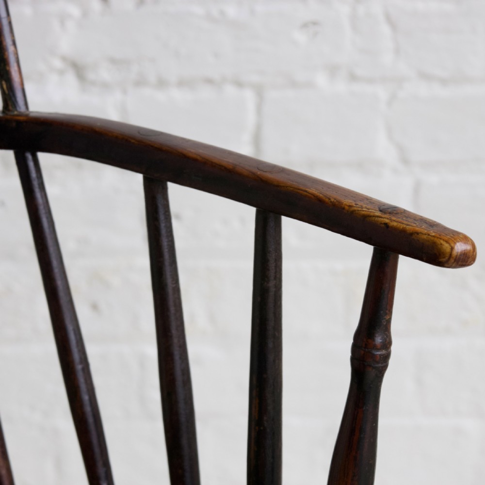 An 18th-century dark brown wooden stickback Windsor armchair featuring a tall curved hoop back, turned legs, and an H-stretcher. View VII
