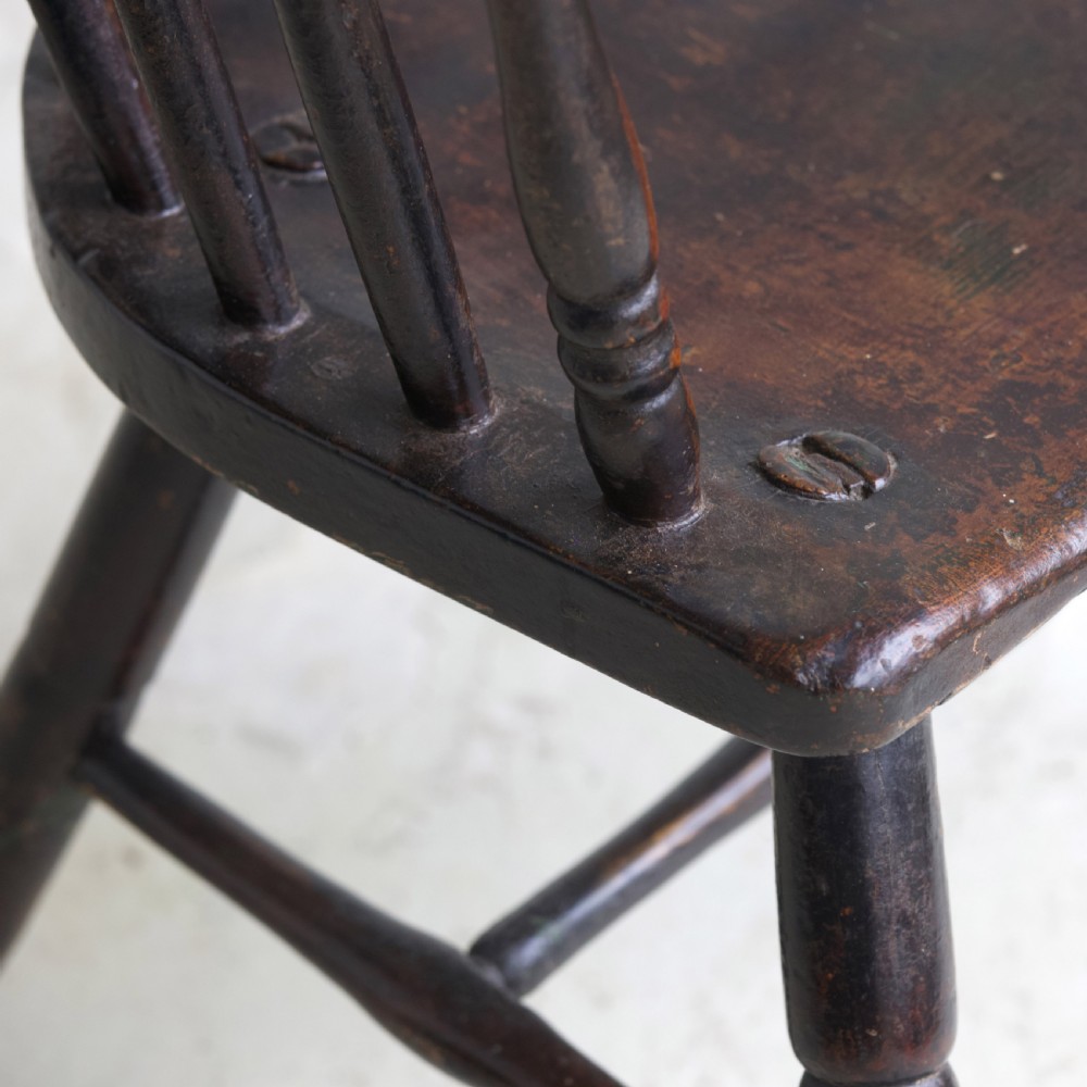 An 18th-century dark brown wooden stickback Windsor armchair featuring a tall curved hoop back, turned legs, and an H-stretcher. View VIII