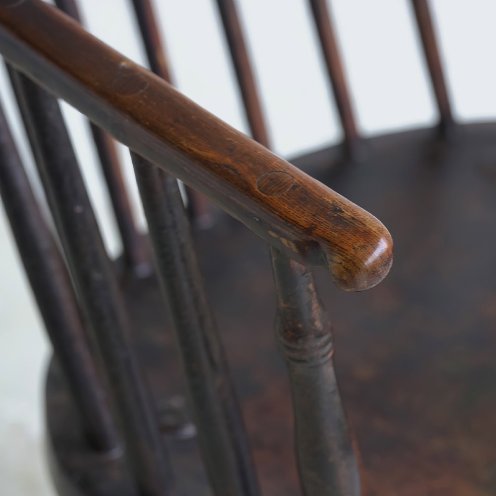 An 18th-century dark brown wooden stickback Windsor armchair featuring a tall curved hoop back, turned legs, and an H-stretcher. View X