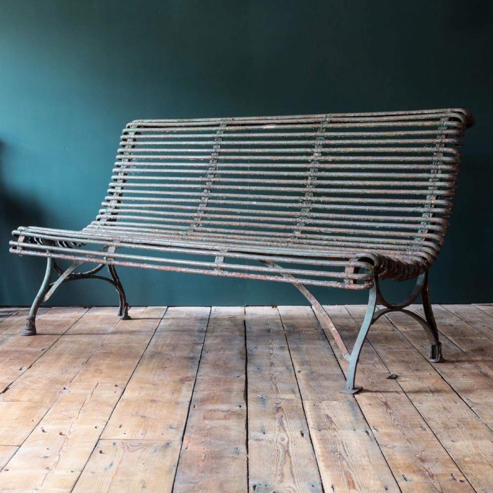 A nineteenth-century French Arras garden bench made of curved green tubular iron slats resting on a riveted iron frame.