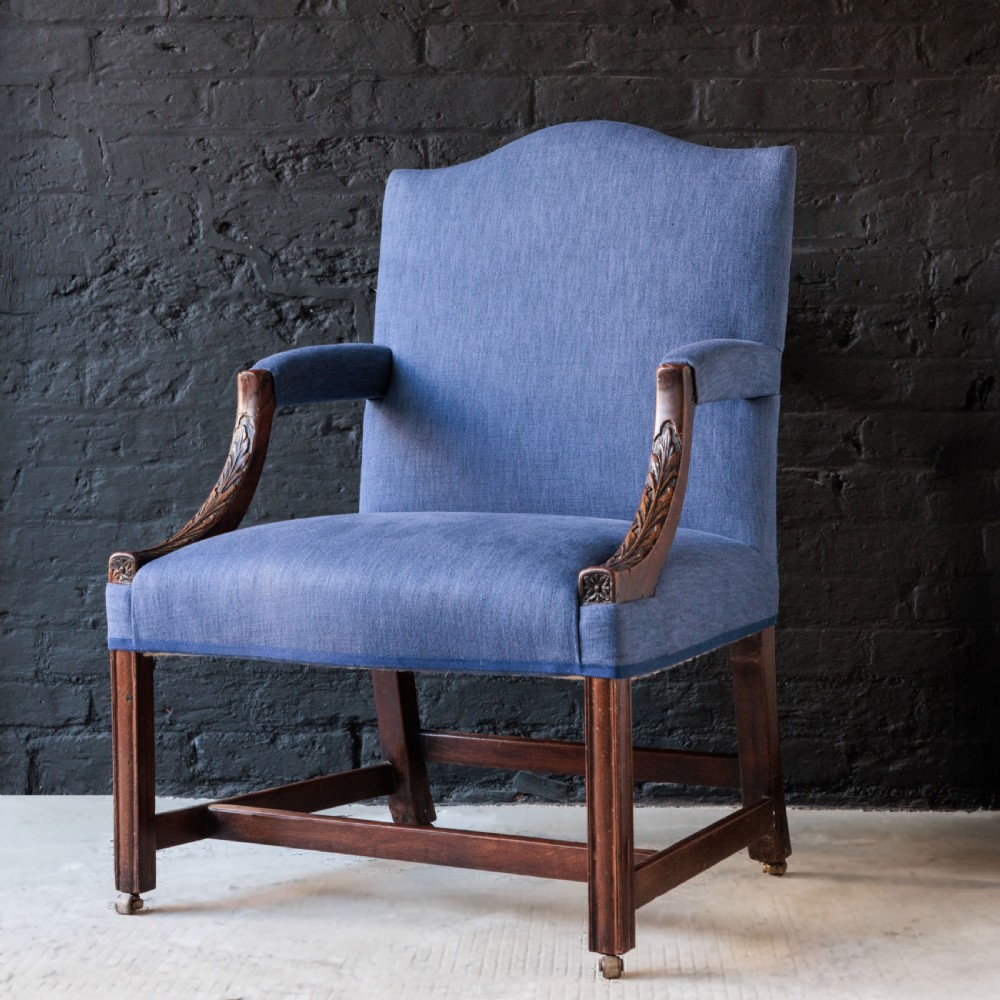 A Georgian Gainsborough armchair with light blue upholstery, carved mahogany arm supports, square stretchered legs, and brass castors.