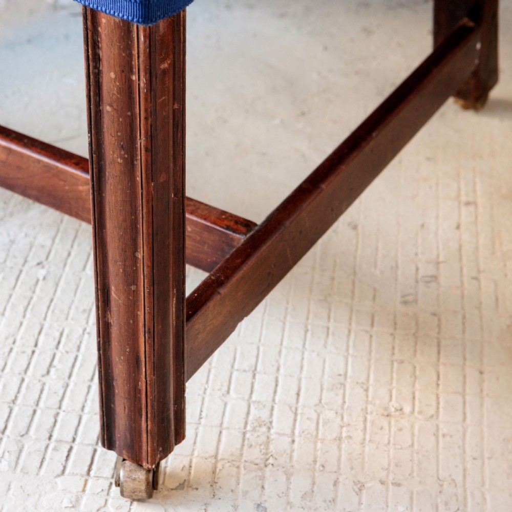 A Georgian Gainsborough armchair with light blue upholstery, carved mahogany arm supports, square stretchered legs, and brass castors. View V