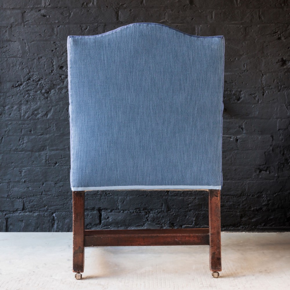 A Georgian Gainsborough armchair with light blue upholstery, carved mahogany arm supports, square stretchered legs, and brass castors. View X