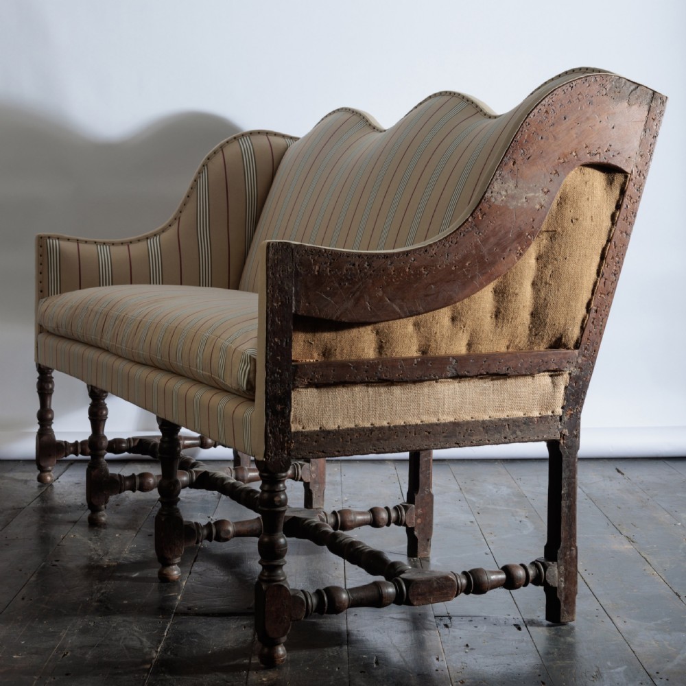 A 17th century wingback sofa featuring striped upholstery, exposed jute side panels, turned wooden legs, and stretchers. View VI