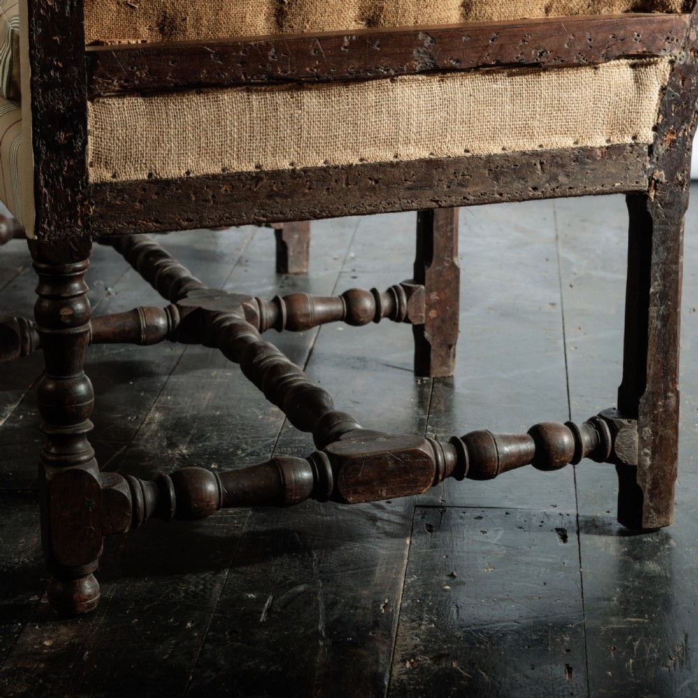 A 17th century wingback sofa featuring striped upholstery, exposed jute side panels, turned wooden legs, and stretchers. View XV