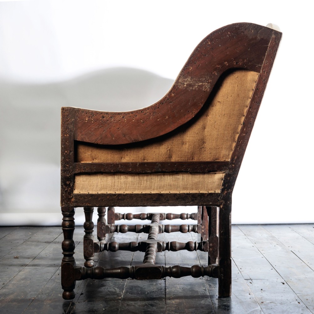 A 17th century wingback sofa featuring striped upholstery, exposed jute side panels, turned wooden legs, and stretchers. View XVII