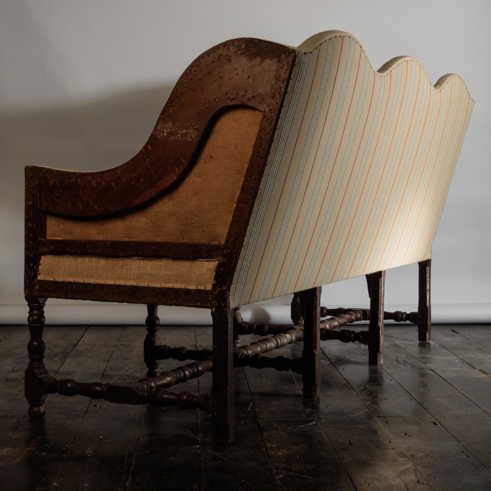 A 17th century wingback sofa featuring striped upholstery, exposed jute side panels, turned wooden legs, and stretchers. View XIX