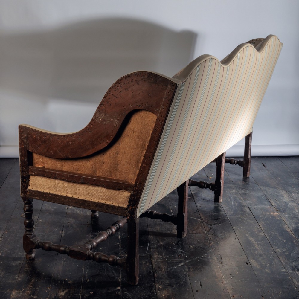 A 17th century wingback sofa featuring striped upholstery, exposed jute side panels, turned wooden legs, and stretchers. View XX