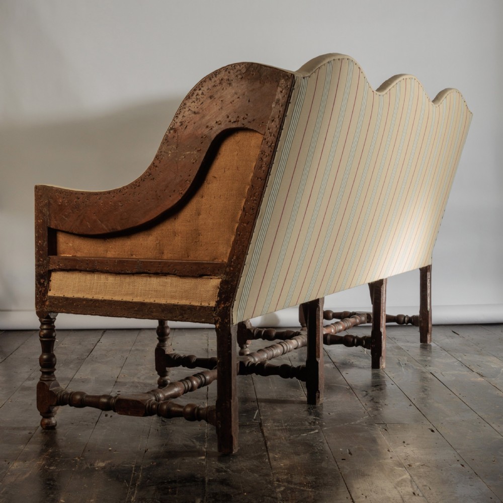 A 17th century wingback sofa featuring striped upholstery, exposed jute side panels, turned wooden legs, and stretchers. View XXI