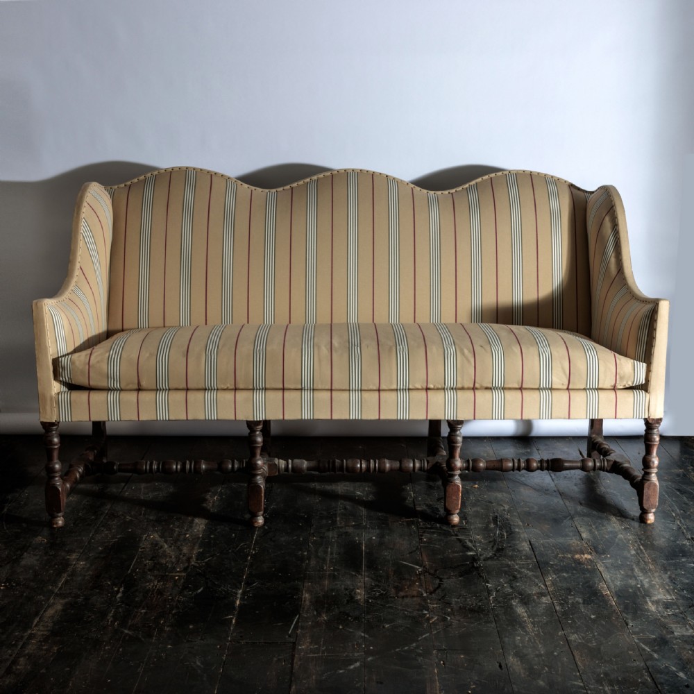 A 17th century wingback sofa featuring striped upholstery, exposed jute side panels, turned wooden legs, and stretchers. View XXIV
