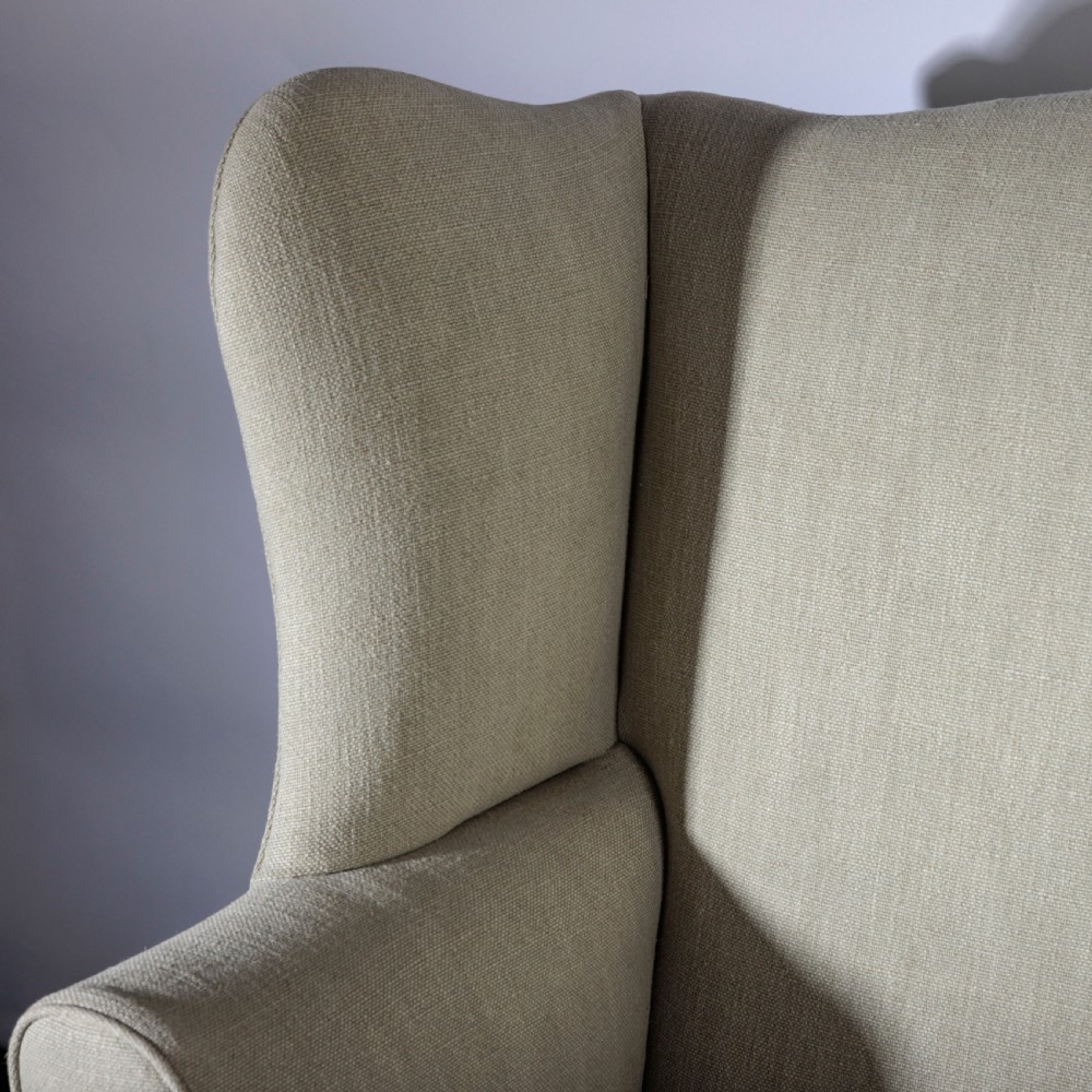 An 18th-century Georgian style wingback armchair upholstered in neutral cream linen, supported by dark square timber legs with H-stretchers. View III