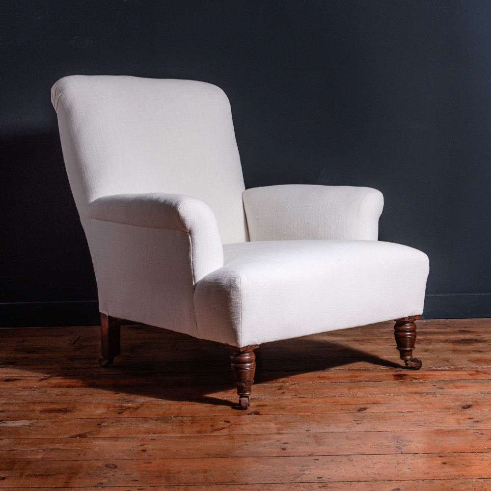 A 19th-century Victorian armchair upholstered in neutral off-white fabric featuring a reclined backrest, padded arms, and turned wooden front legs on castors.