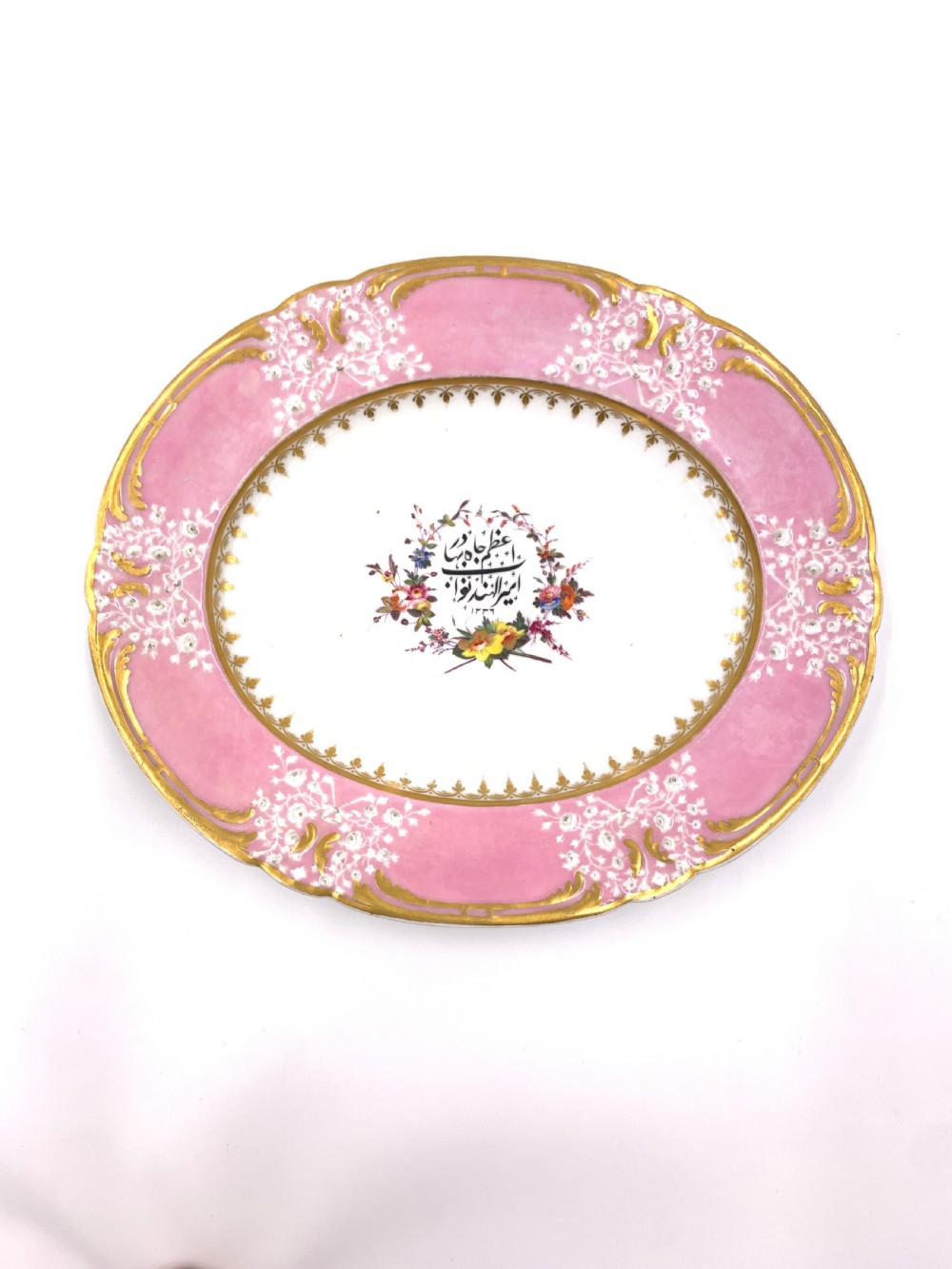 A set of six Regency porcelain plates and platters with rose pink borders, burnished gilding, and central script inscriptions framed by floral wreaths. View II