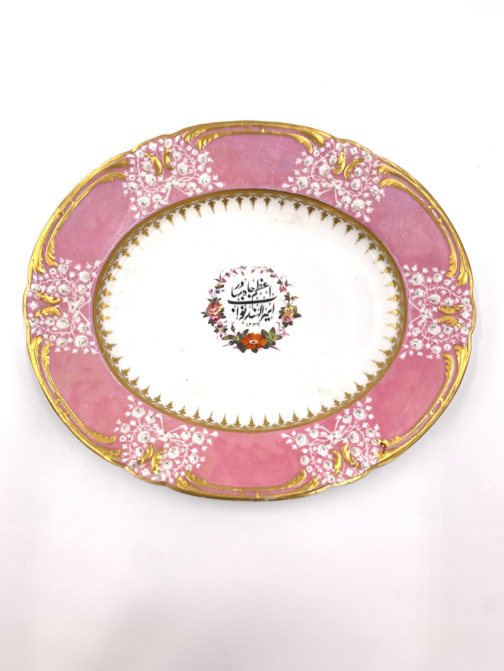 A set of six Regency porcelain plates and platters with rose pink borders, burnished gilding, and central script inscriptions framed by floral wreaths. View V