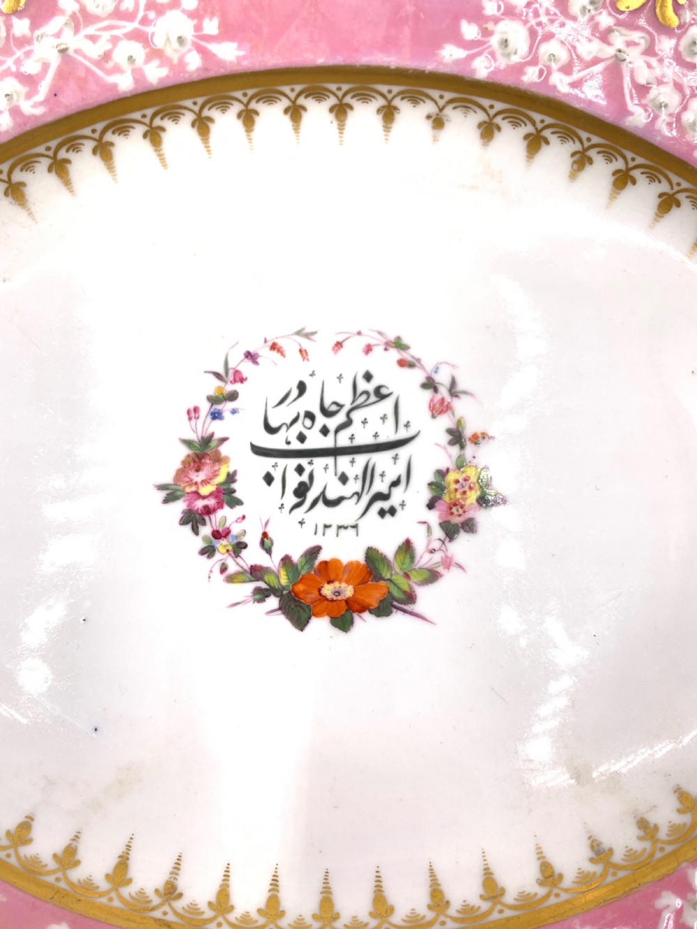 A set of six Regency porcelain plates and platters with rose pink borders, burnished gilding, and central script inscriptions framed by floral wreaths. View VI