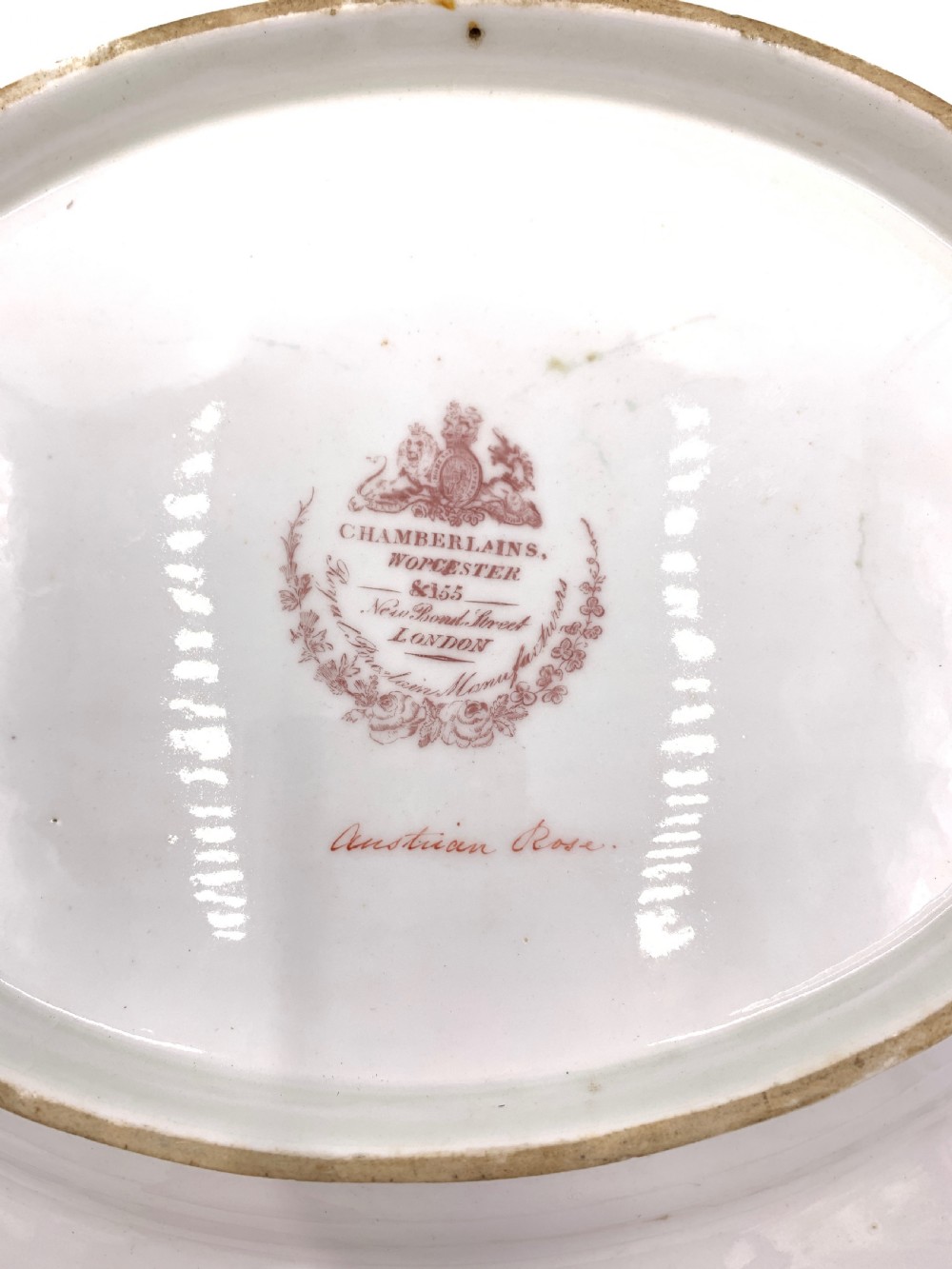 A set of six Regency porcelain plates and platters with rose pink borders, burnished gilding, and central script inscriptions framed by floral wreaths. View VII