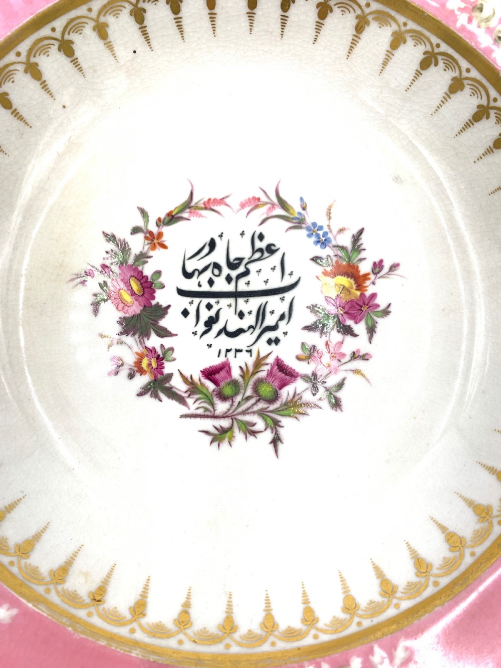 A set of six Regency porcelain plates and platters with rose pink borders, burnished gilding, and central script inscriptions framed by floral wreaths. View IX