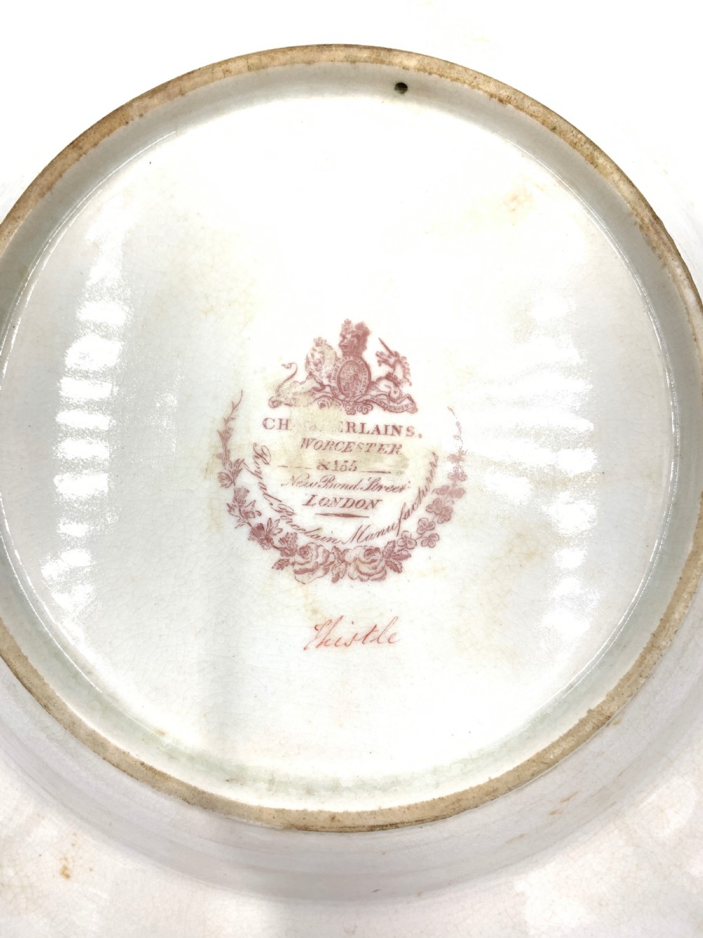 A set of six Regency porcelain plates and platters with rose pink borders, burnished gilding, and central script inscriptions framed by floral wreaths. View X