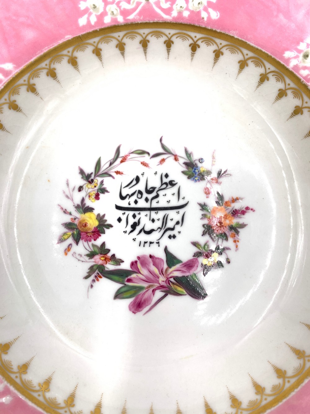 A set of six Regency porcelain plates and platters with rose pink borders, burnished gilding, and central script inscriptions framed by floral wreaths. View XII