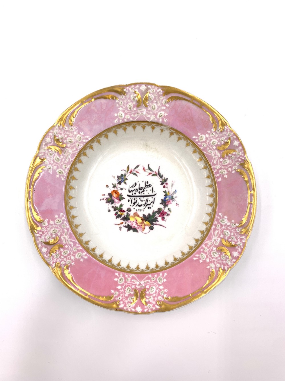 A set of six Regency porcelain plates and platters with rose pink borders, burnished gilding, and central script inscriptions framed by floral wreaths. View XIV