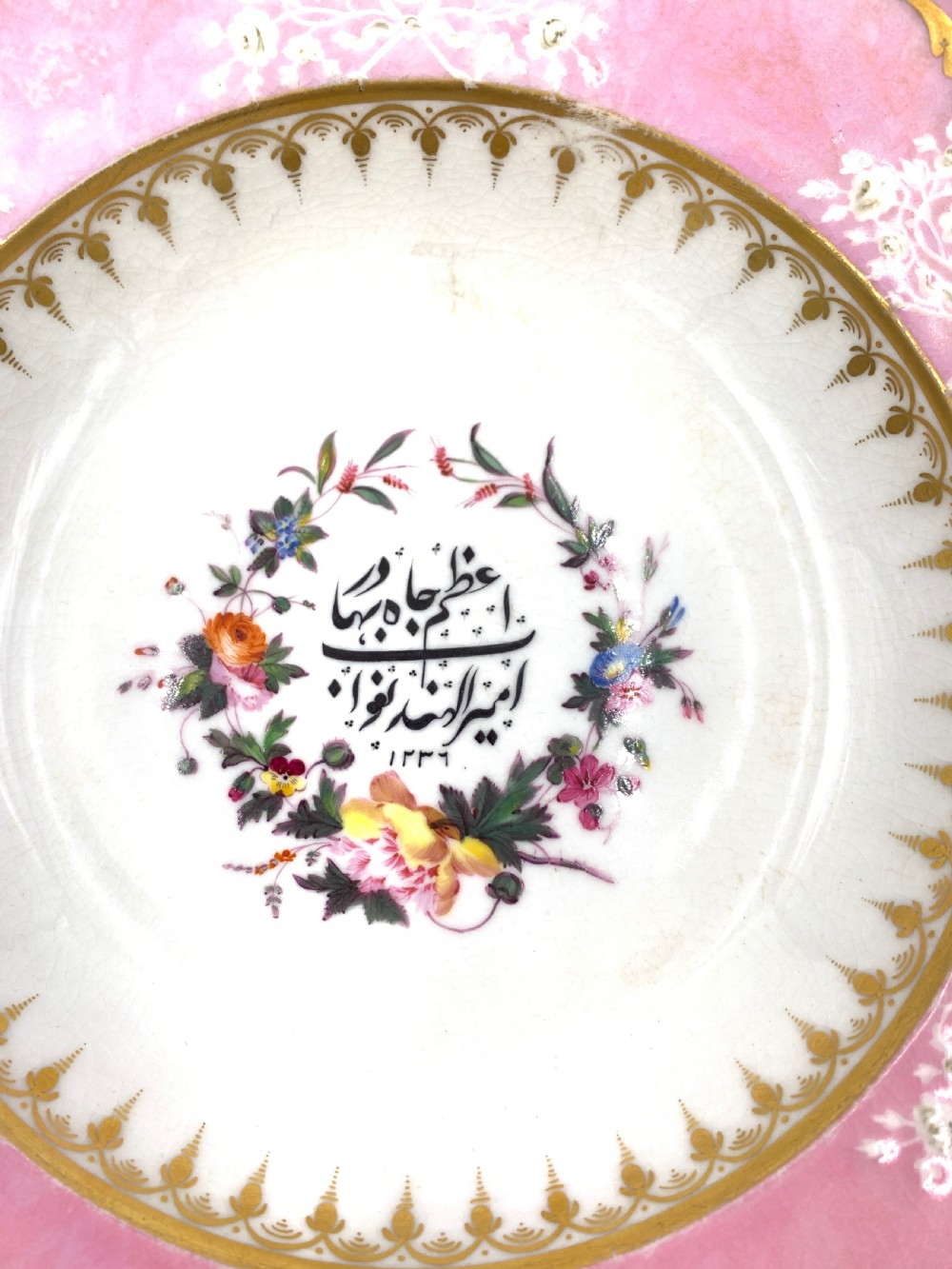 A set of six Regency porcelain plates and platters with rose pink borders, burnished gilding, and central script inscriptions framed by floral wreaths. View XV