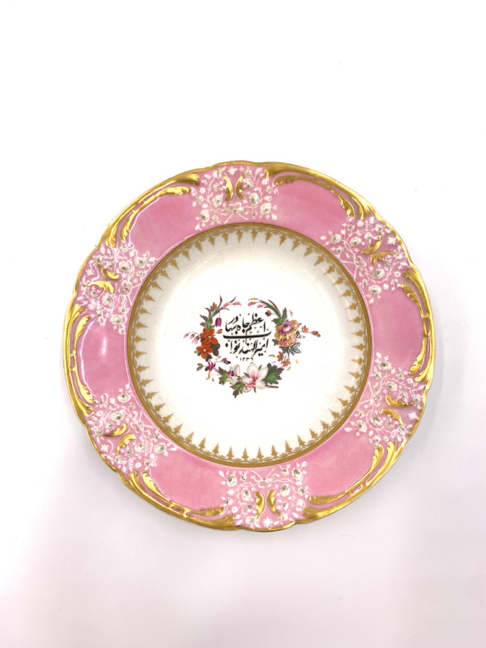 A set of six Regency porcelain plates and platters with rose pink borders, burnished gilding, and central script inscriptions framed by floral wreaths. View XVII
