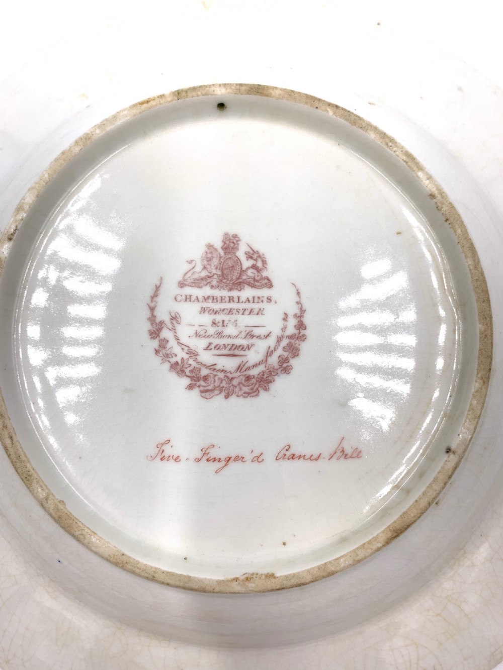 A set of six Regency porcelain plates and platters with rose pink borders, burnished gilding, and central script inscriptions framed by floral wreaths. View XIX