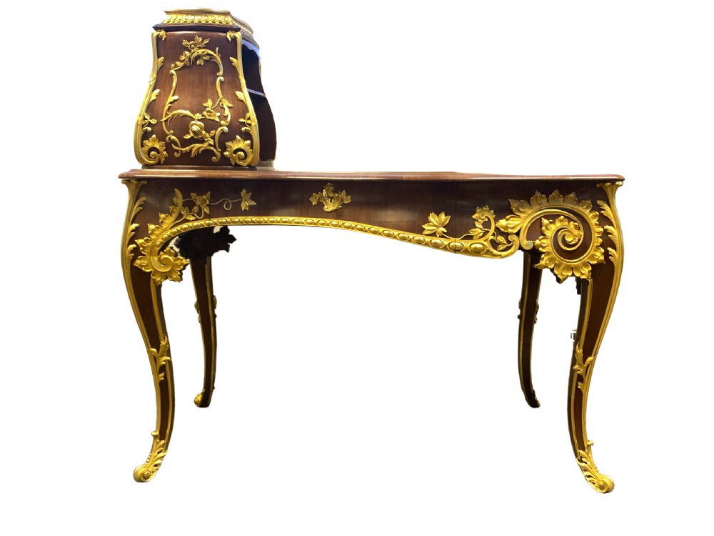 A 19th-century dark wood writing desk featuring elaborate gilt-bronze floral ormolu mounts, cabriole legs, and an asymmetrical raised side superstructure.