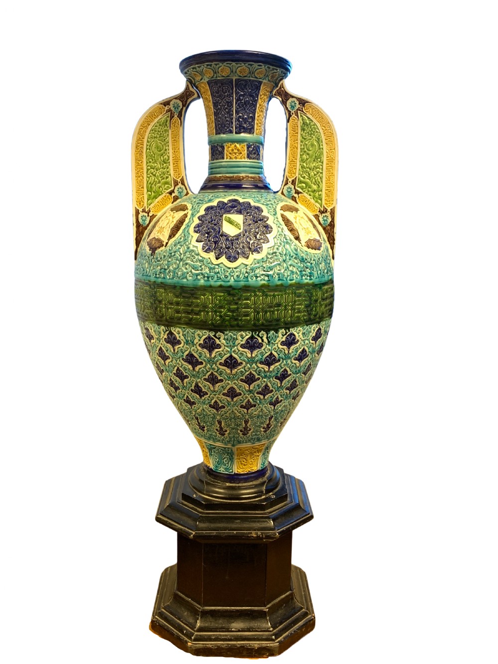 A tall 19th-century Alhambra-style ceramic vase featuring winged handles, arabesque relief decoration, and turquoise and cobalt glazes on an octagonal black base.