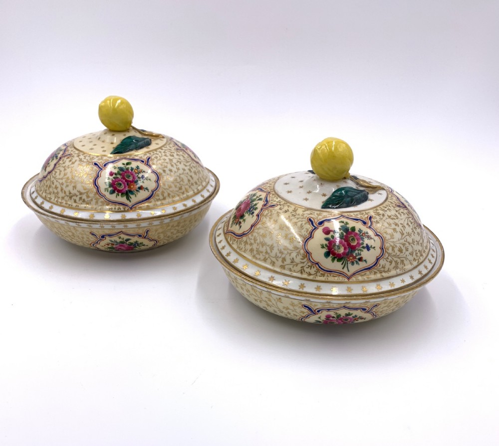 A pair of circular porcelain bonbonnieres featuring cream ground with gold leaf scrollwork, hand-painted floral cartouches, and sculpted lemon finials on the lids. View II