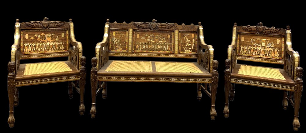 A three-piece nineteenth-century Egyptian Revival furniture suite consisting of a settee and two armchairs with carved winged crestings, figural marquetry backrests, and cane seats.